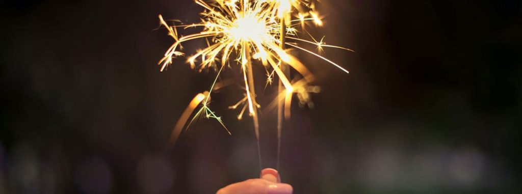 A dark background with a hand holding sparklers