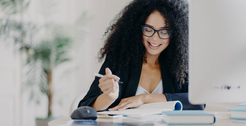 A woman wearing glasses holding a pen and a notebook