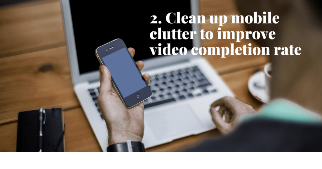 a hand holding a mobile phone with a laptop in the background
