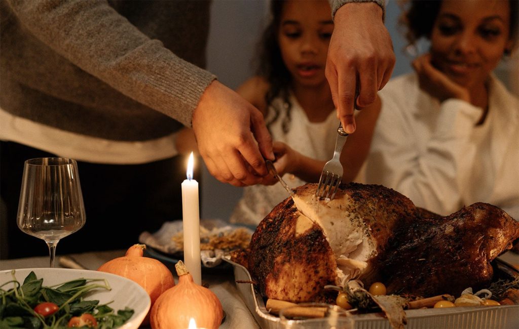 someone carving a turkey on a decorated table with two people watching in the background