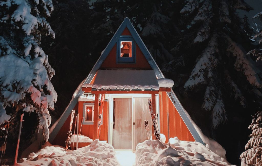 a cottage home lit up at night surrounded by snowy trees
