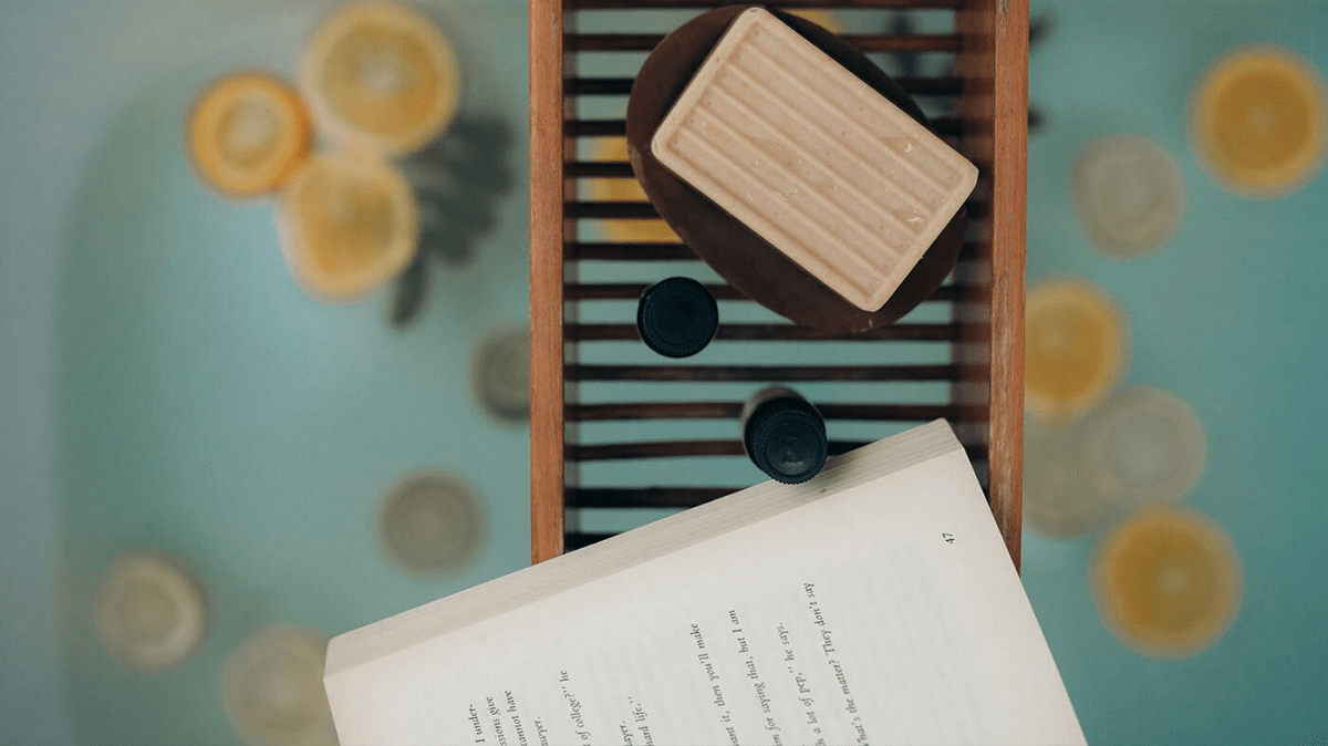 A top down view of a bath full of lemons with a tray holding a book and a bar of soap