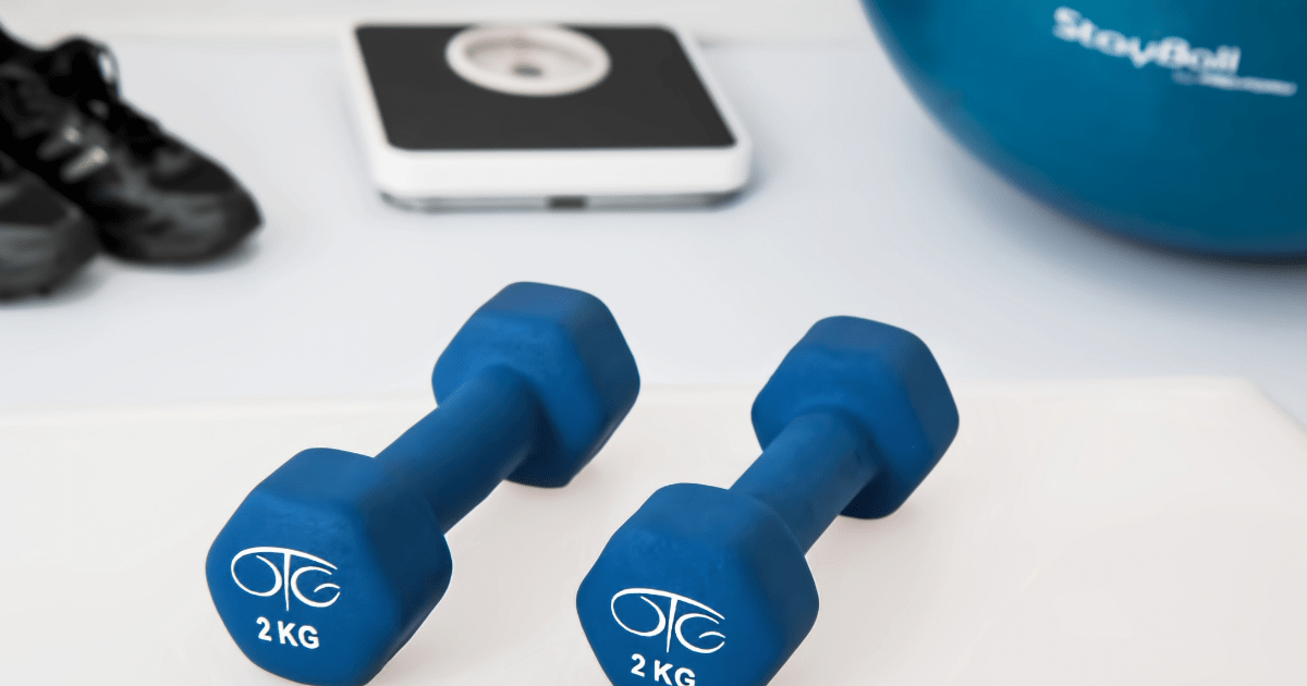 two hand weights and a scale, workout shoes and a workout ball in the background
