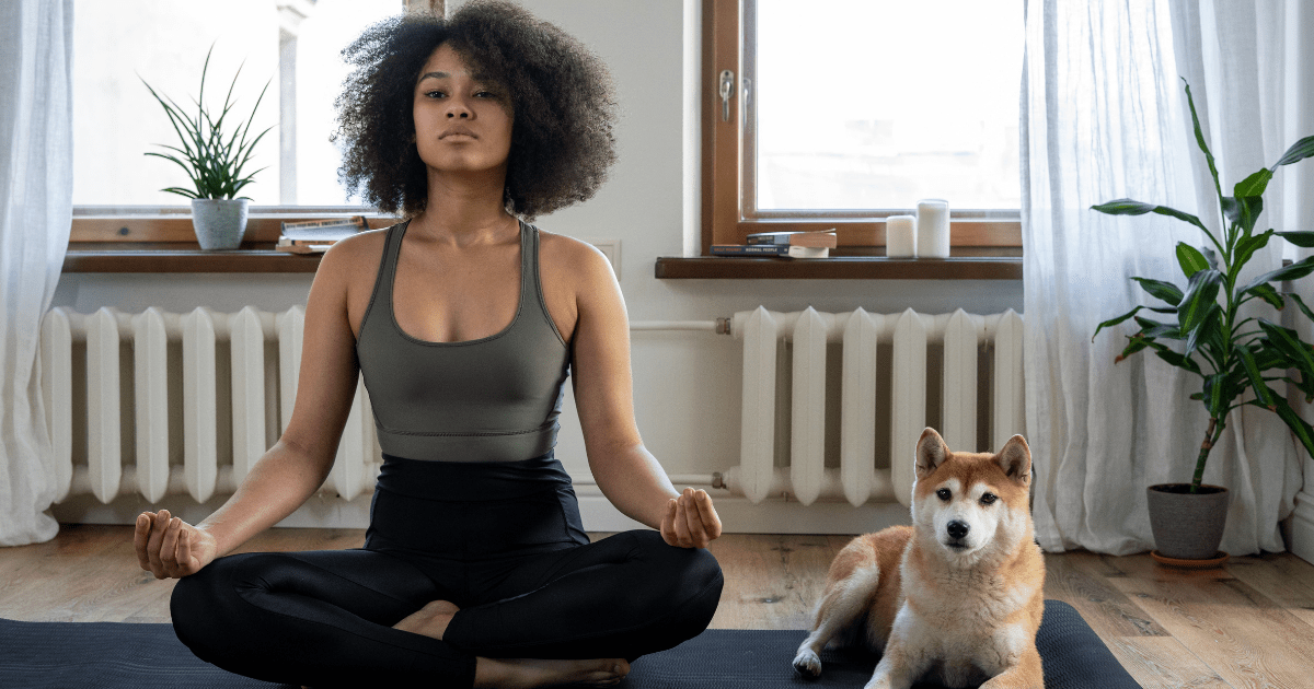 a woman sitting in a yoga pose on a mat with her dog next to her