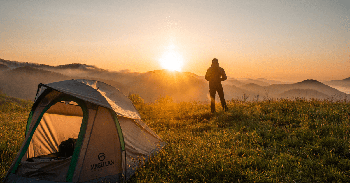 tent in the wilderness with man looking at a sunrise