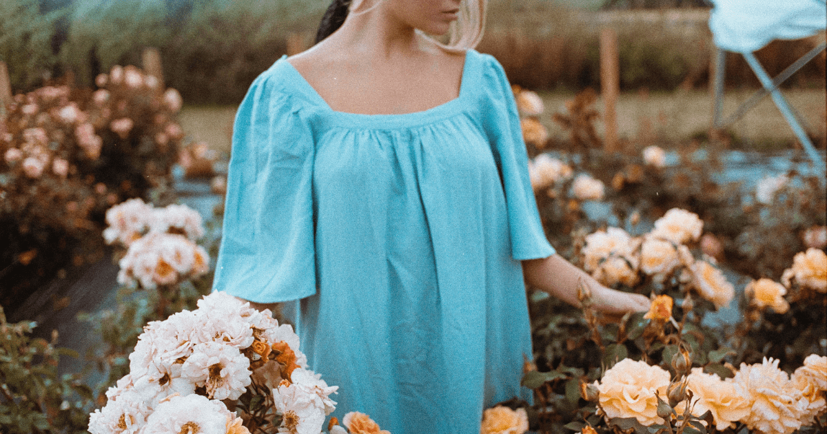 woman in a field of flowers wearing a blue flowy top