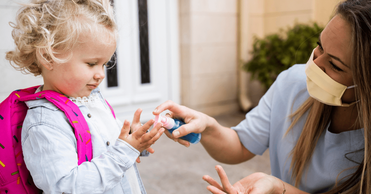 mom giving a young girl hand sanitizer and wearing a mask