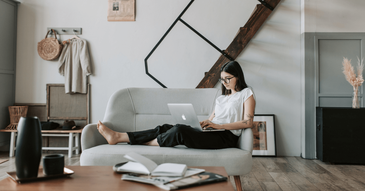 a woman sitting on a couch working on a laptop in a modernly decorated room