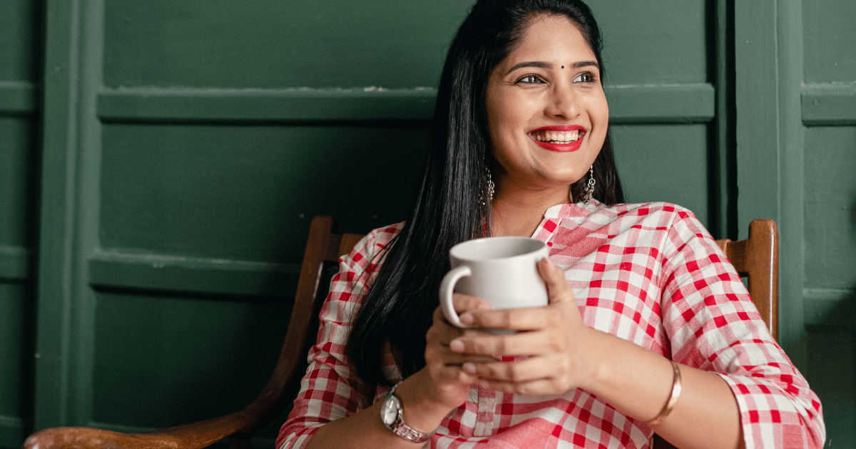 a smiling woman holding a mug and sitting in a chair