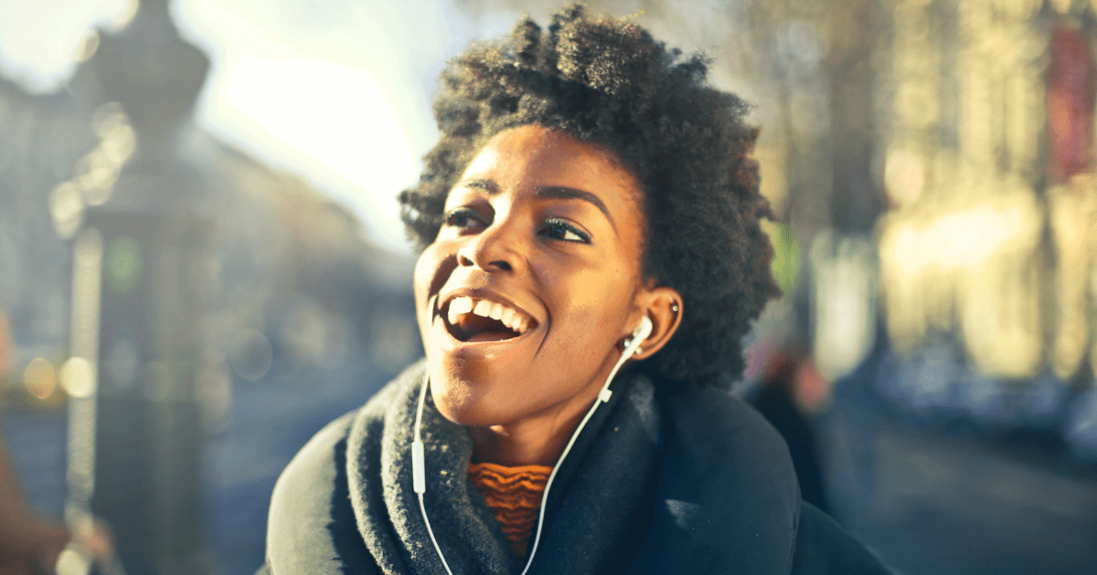 a woman smiling with head phones in and blurred outdoor background