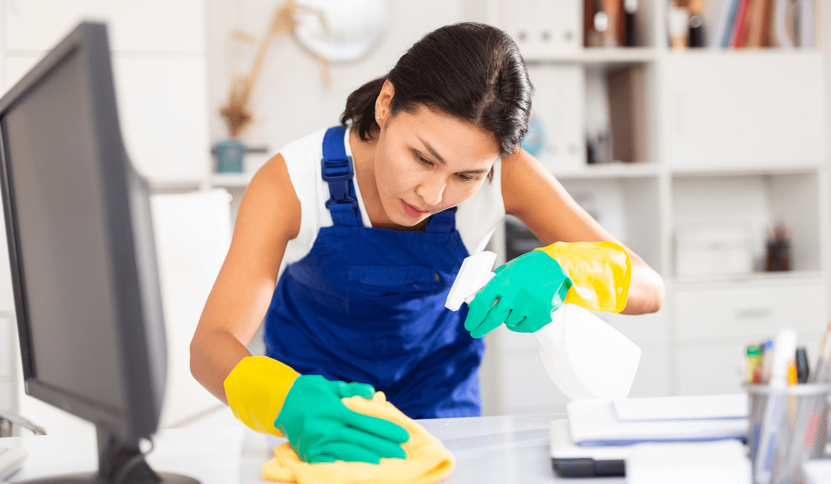 woman wearing cleaning gloves and apron spraying and wiping a surface