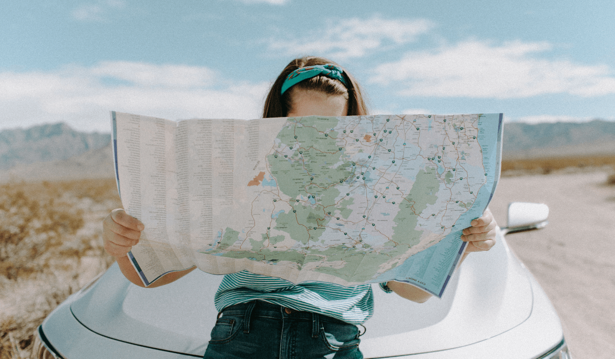 girl looking at a map sitting on the hood of a car