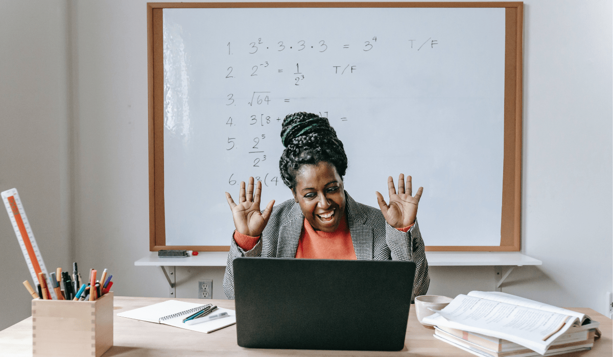 teacher smiling at a computer sitting at a desk