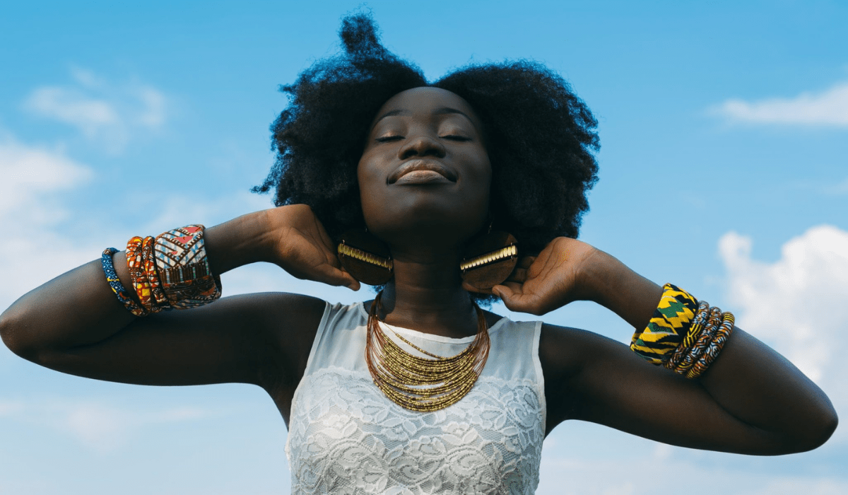 Black woman smiling in the sun with colorful earrings and bracelets