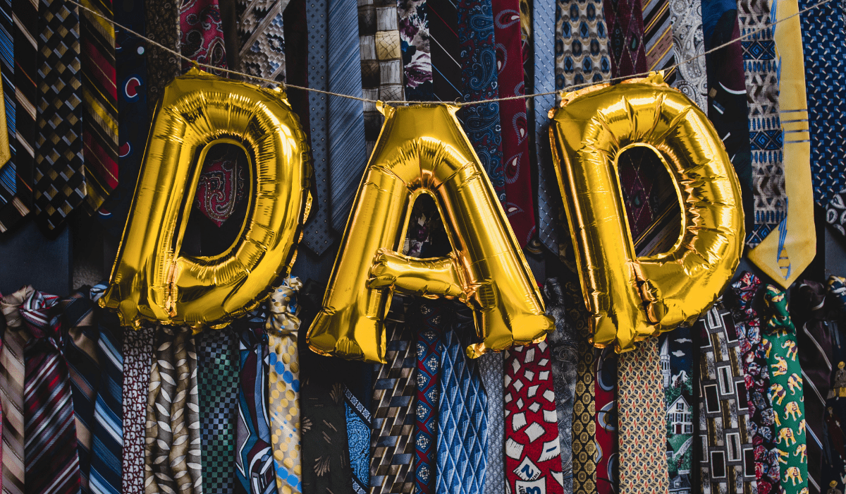 gold balloons spelling out dad set against a bunch of ties for a background