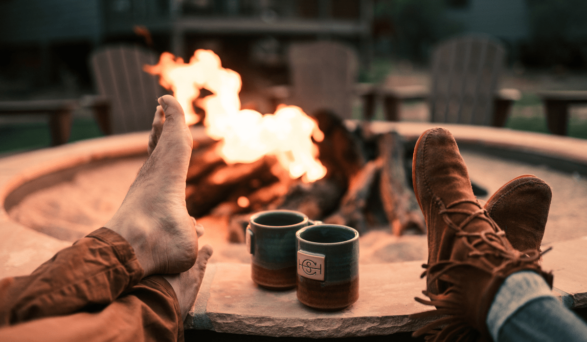 two pairs of feet kicked up on an outdoor fire pit