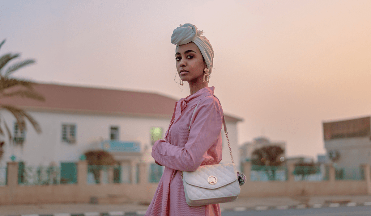 woman outside wearing a pink shirt, fun earrings, and a head piece