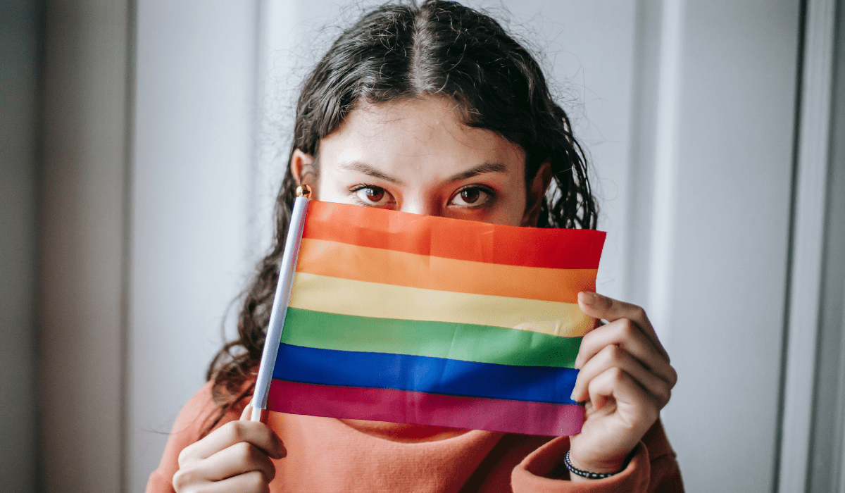 person holding a rainbow flag up, covering half their face