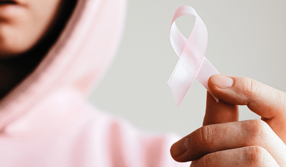 close up pic of a hand holding a pink breast cancer awareness ribbon