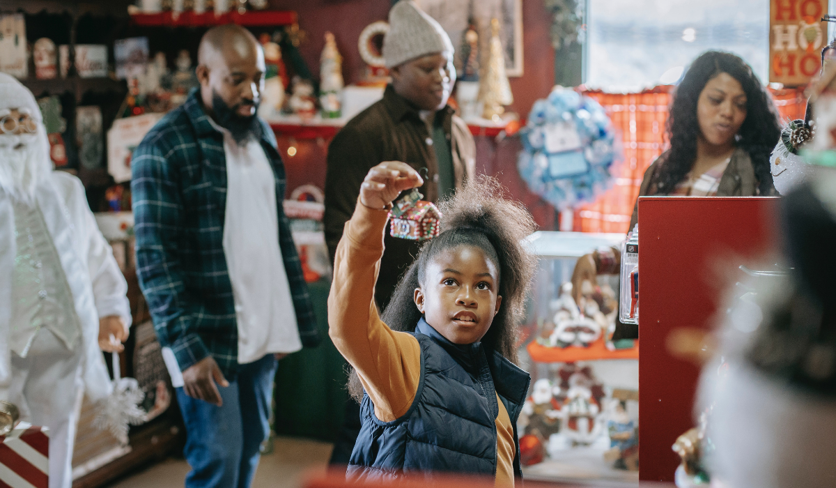 girl holding up a gingerbread house ornament