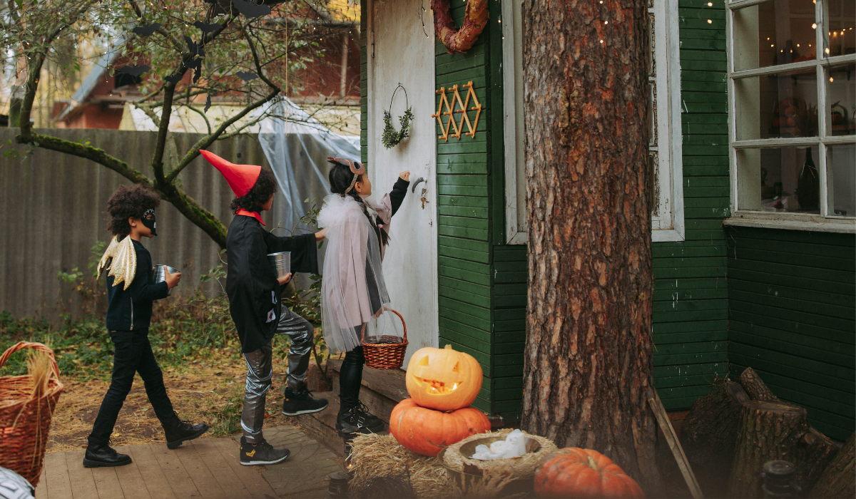 three kids in costumes knocking on a door trick or treating