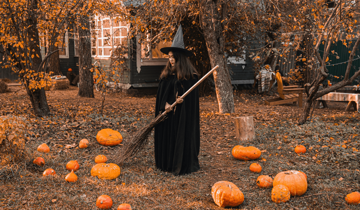 woman in a witch costume holding a broom with pumpkins all around