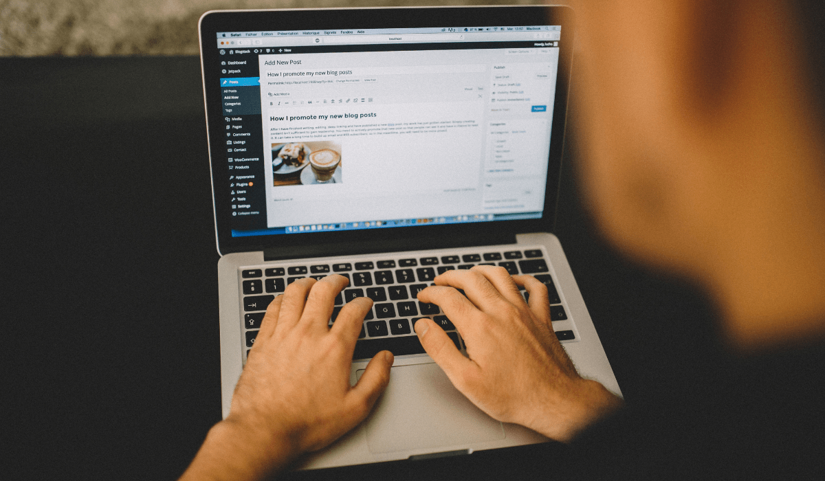 Closeup of hands typing on a keyboard and the screen showing blog post production