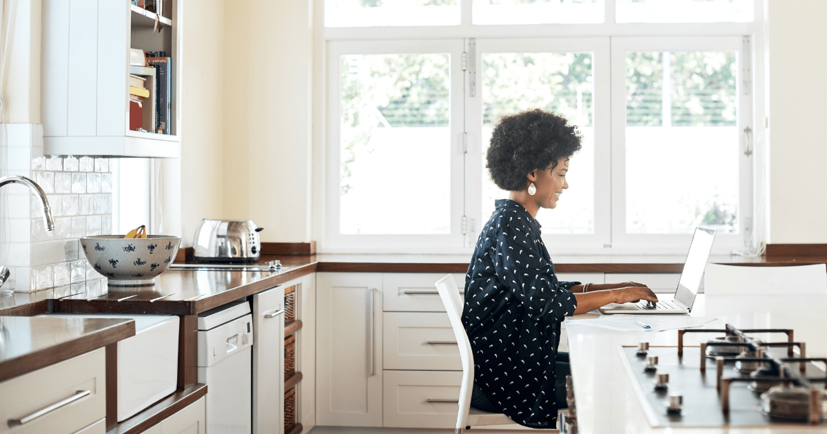 A woman sitting at her kitchen counter working on laptop