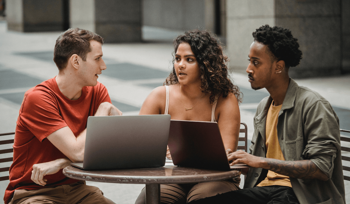 Three people sitting at an outdoor table with laptops