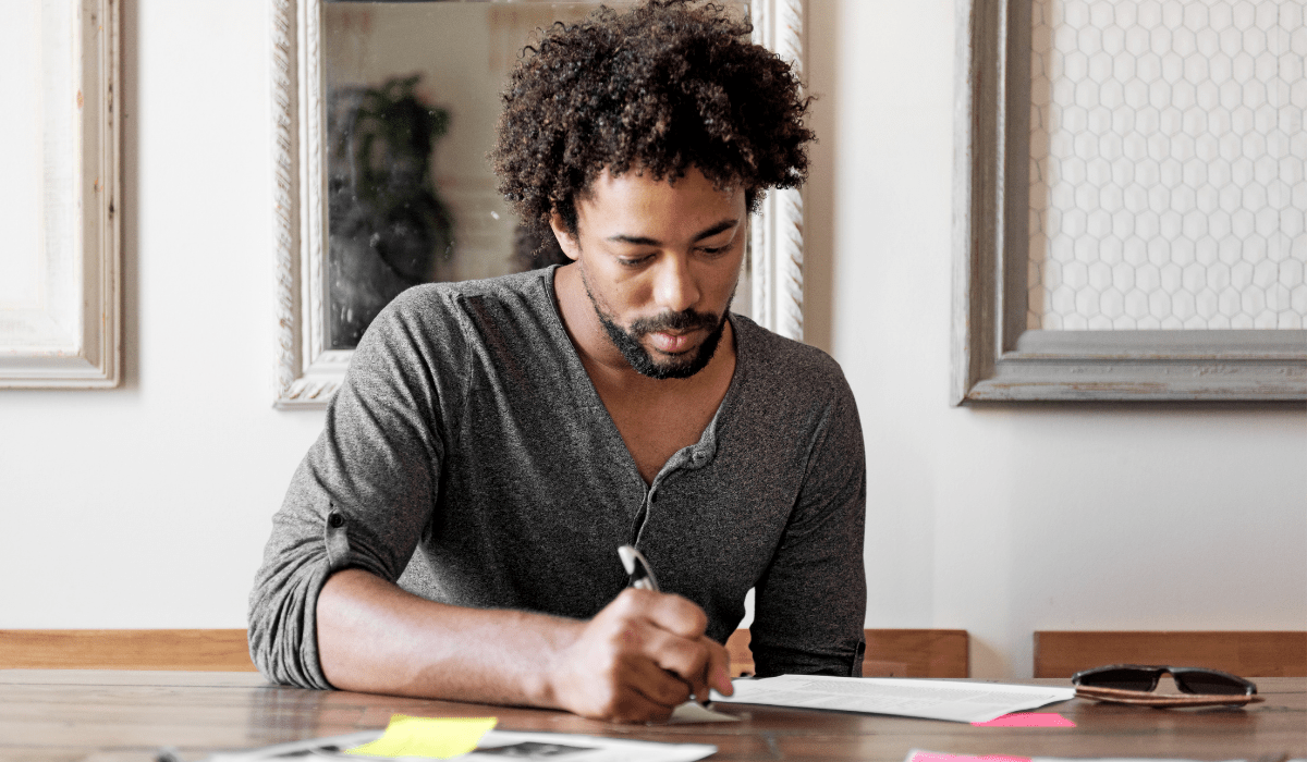 Man working at a table holding a pen and writing on paper