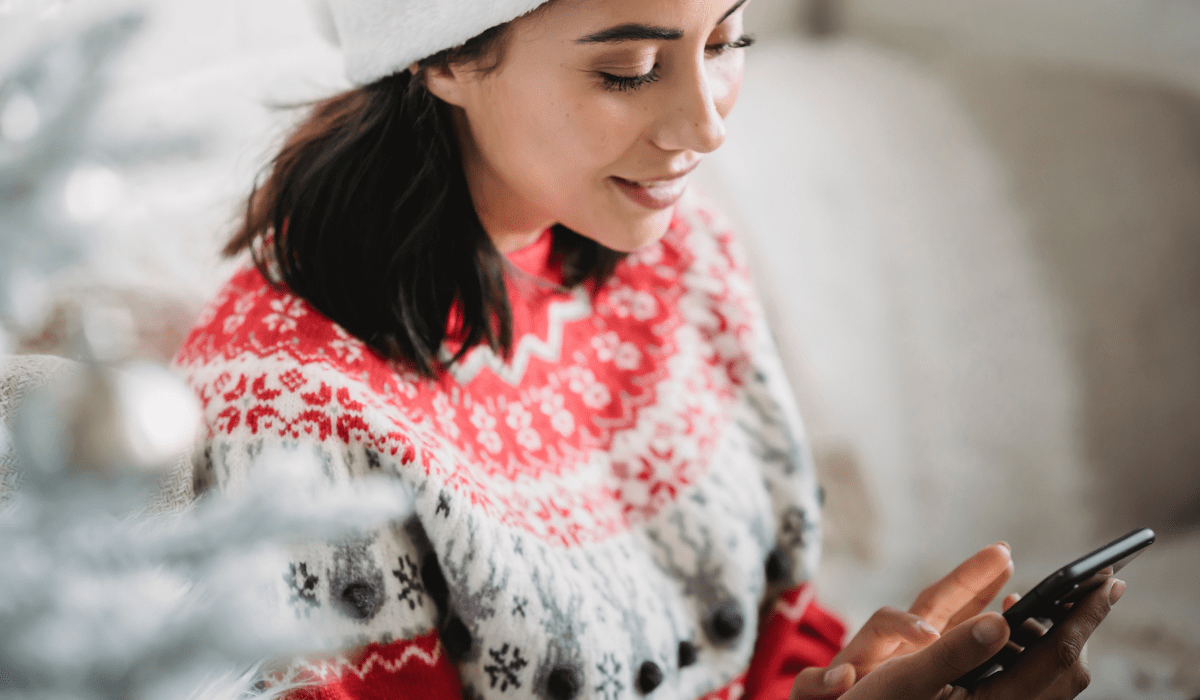 A lady looking down at her phone wearing a winter sweater and hat