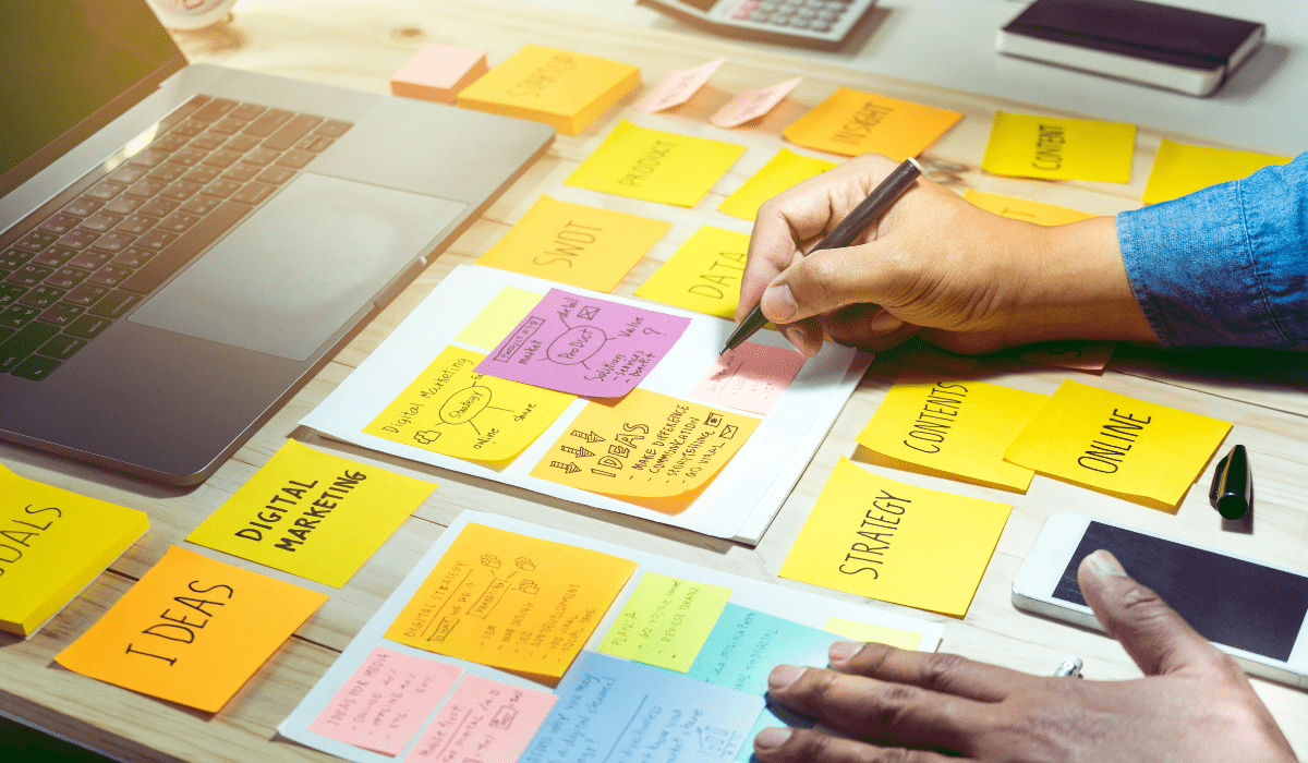 A top down view of a desk with a ton of sticky notes and a hand writing notes