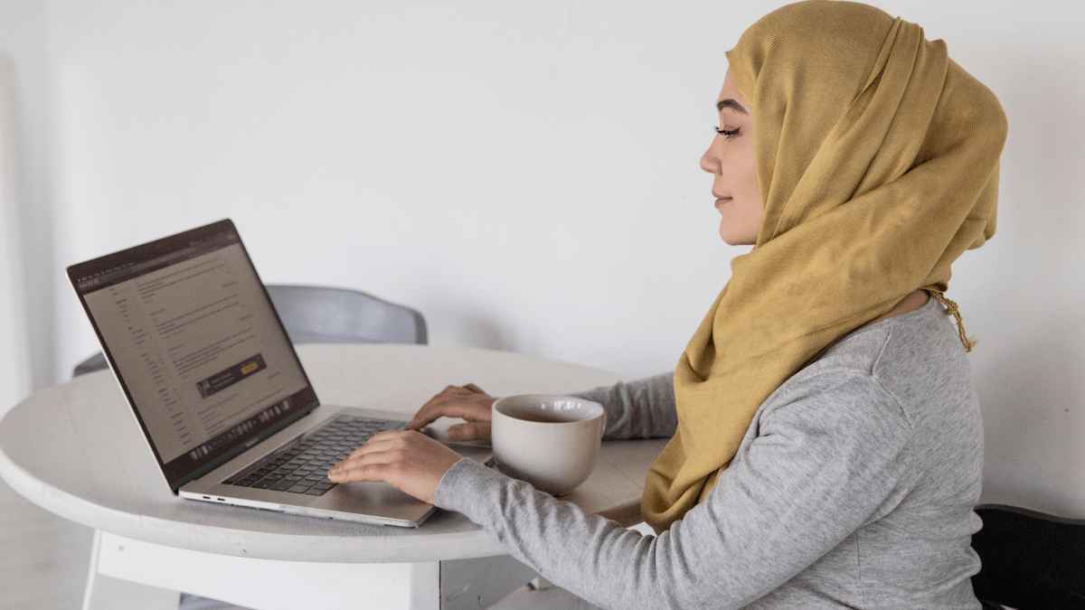 Person sitting at a table working on a laptop with a cup of coffee or tea